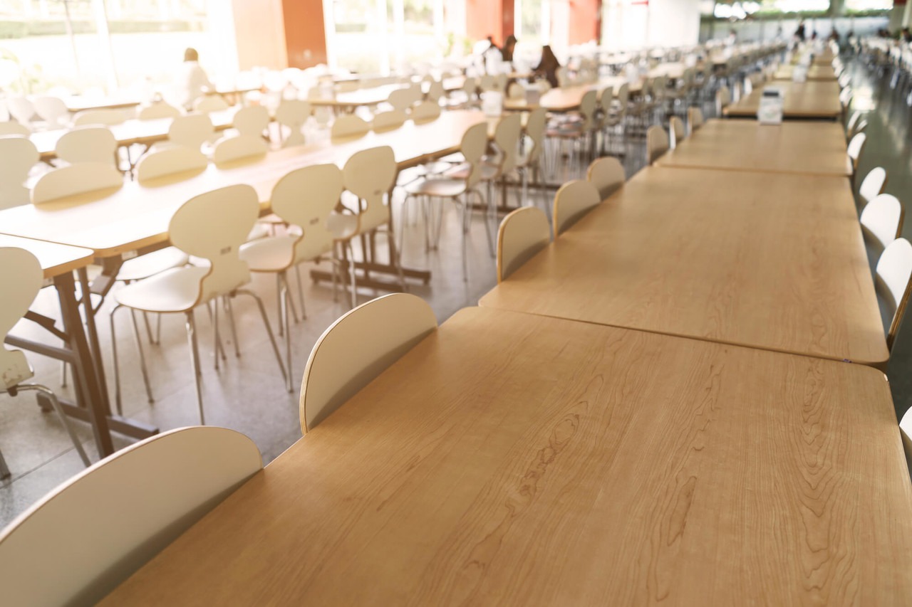 Birleştirilmiş masaların ve sandalyelerin olduğu bir yemekhane